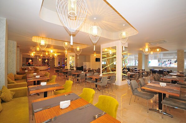 A modern restaurant with multiple dining areas, including a bar and a seating area with yellow chairs.
