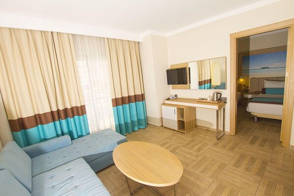 Habitación de hotel con sofá, una mesita redonda, escritorio con silla, televisor y cama.