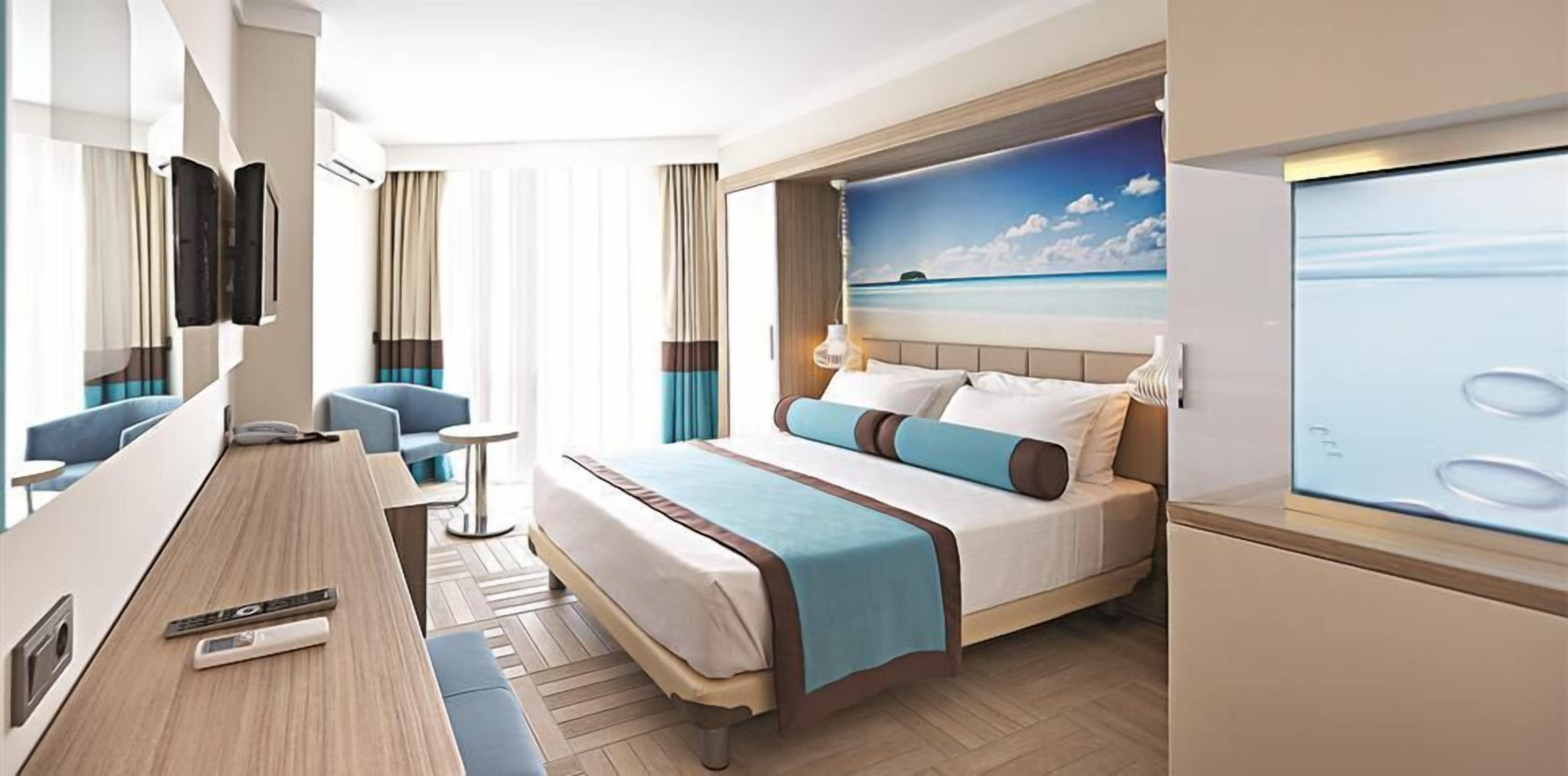 Habitació d'hotel moderna amb llit, escriptori, cadira i finestra gran amb vista al mar.