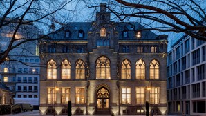 A historic building with arched windows and a central entrance, surrounded by a courtyard with benches and a statue. - THE QVEST hideaway (Cologne)