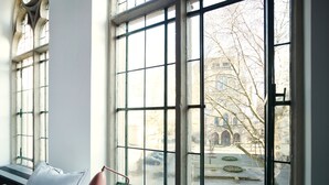 A room with large windows, a radiator, and a chair with a pillow. - THE QVEST hideaway (Cologne)