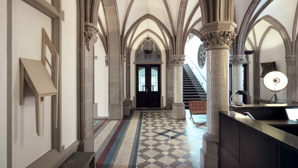 A grand hallway with high arched ceilings, a checkered floor, and a staircase leading to a dark door. - THE QVEST hideaway (Cologne)