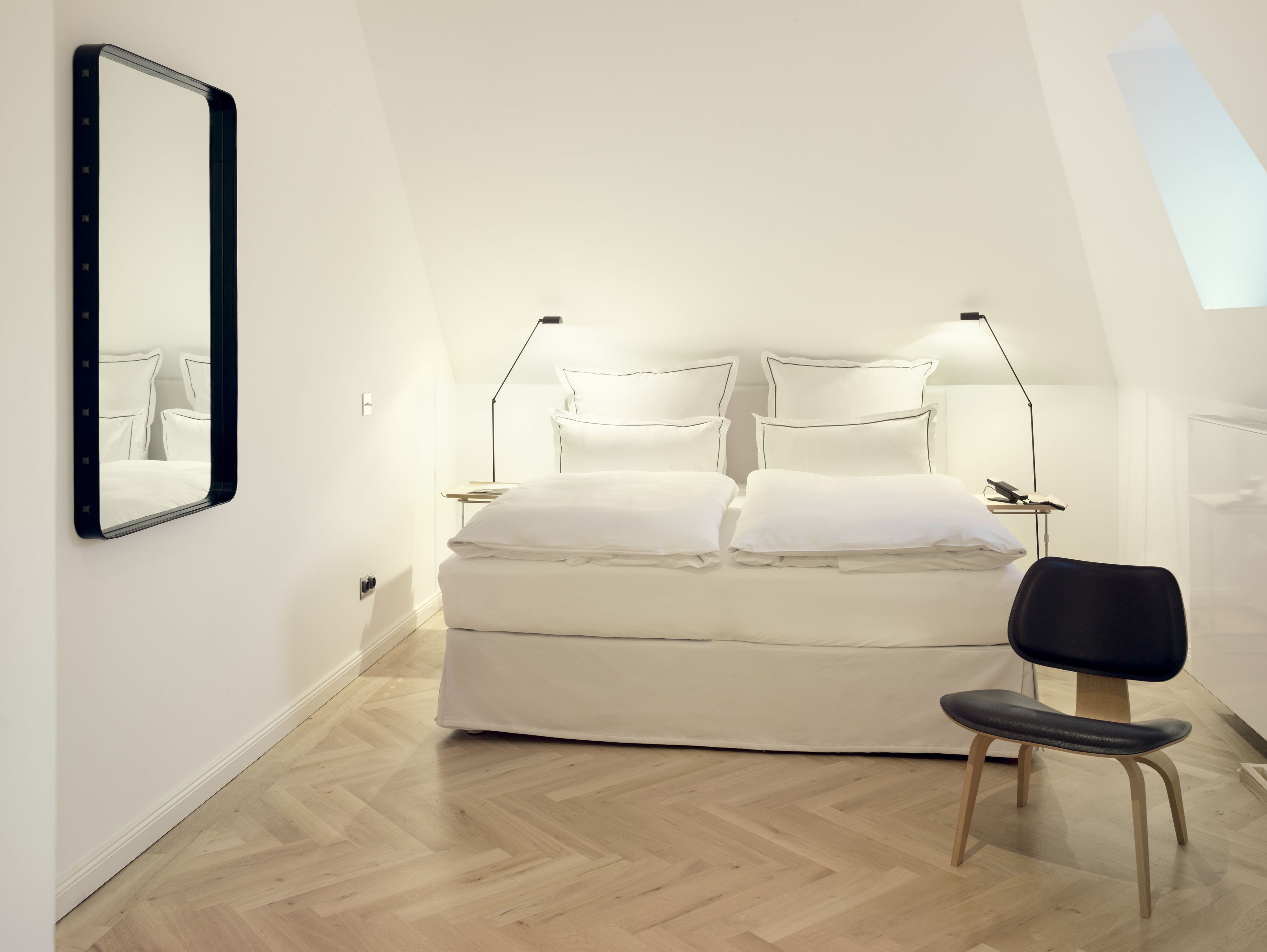 A bedroom with a bed, bedside lamps, a chair, and a mirror on the wall.
