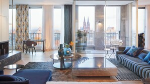 A modern living room with a sofa, a coffee table, and a view of a cityscape through large windows. - THE QVEST hideaway (Cologne)
