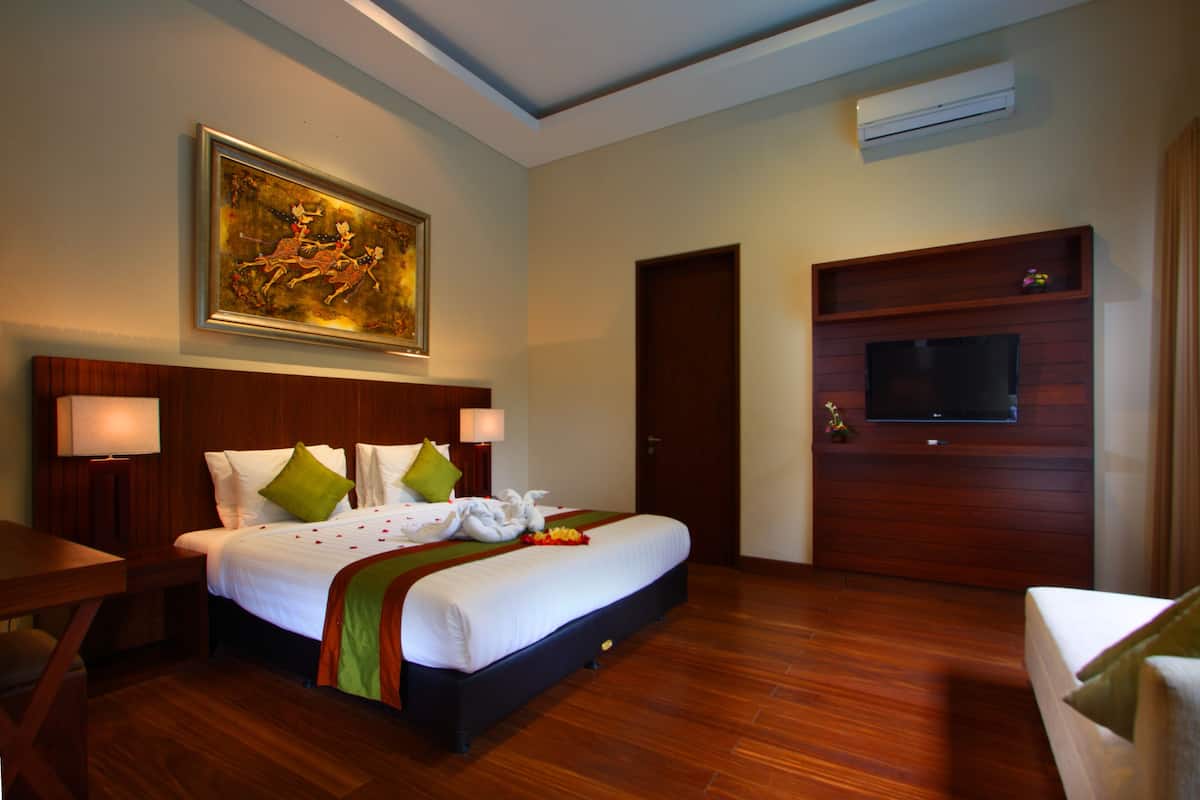Habitación de hotel con una cama grande, un televisor montado en la pared, piso de madera y un cuadro sobre la cama.