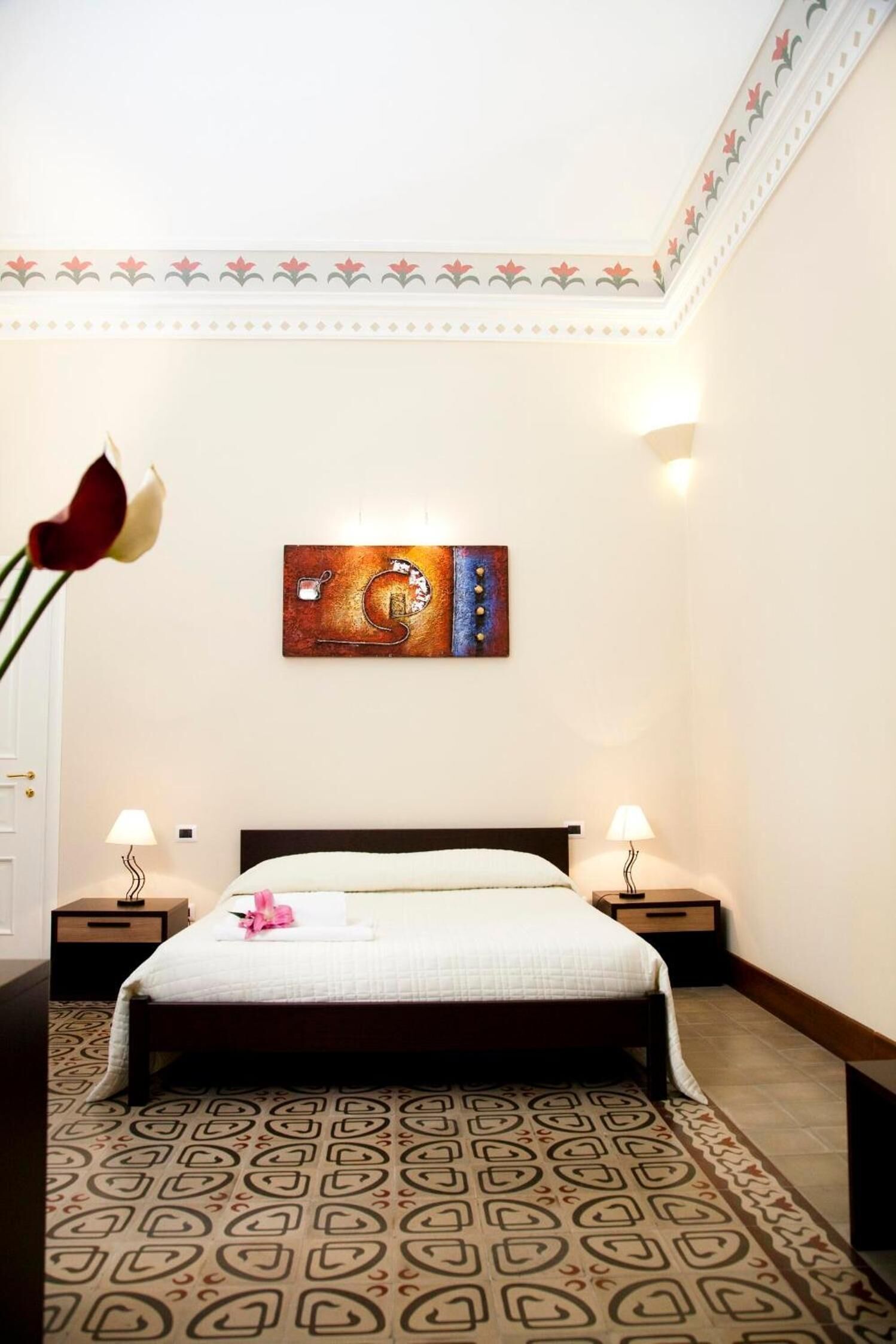 A hotel room with a bed, two bedside tables, a wall-mounted artwork, and a patterned floor.