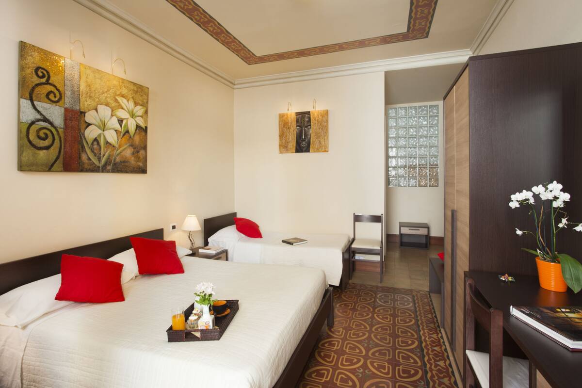 A hotel room with two beds, a desk, a chair, and artwork on the walls.