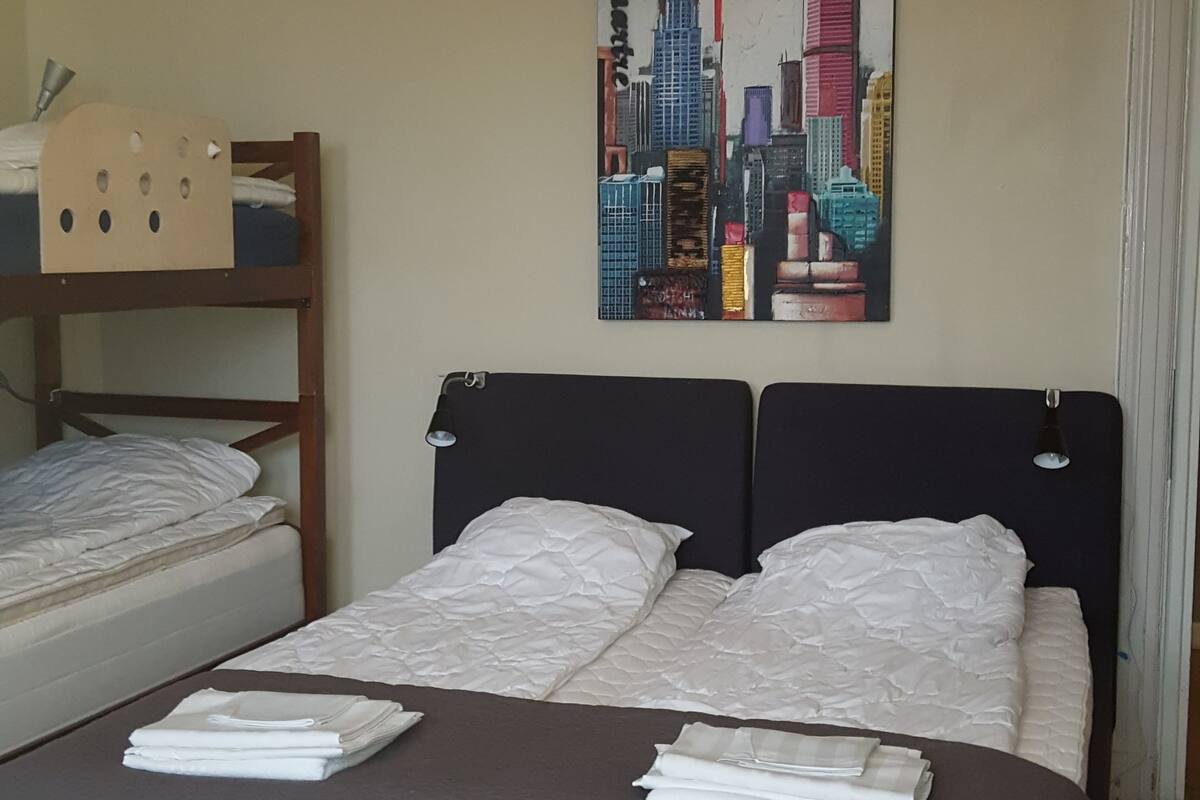Ein Hotelzimmer mit Etagenbett, einem Einzelbett, einem Stadtbildgemälde an der Wand und einer Deckenleuchte.