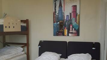 A hotel room with a bunk bed, a single bed, a cityscape painting on the wall, and a ceiling light fixture.