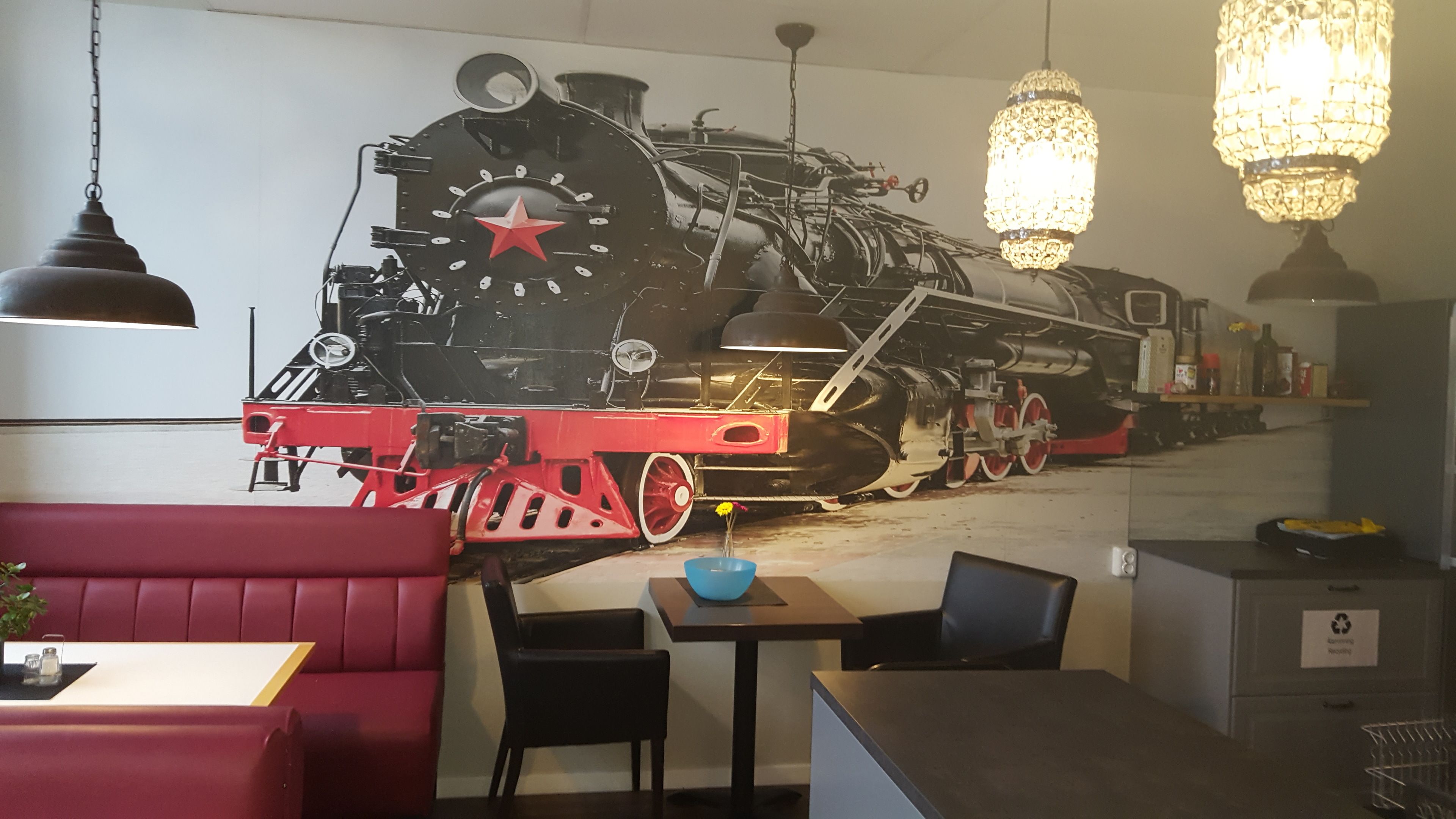 Un restaurant décoré d’une fresque représentant un train, avec des sièges rouges et des luminaires suspendus.