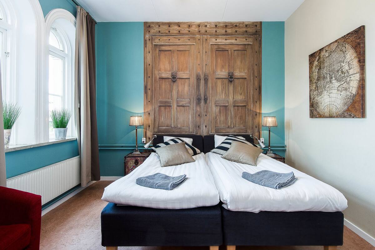 Ein Doppelbett mit weißer Bettwäsche, ein Holzschrank und eine Weltkarte an der Wand.