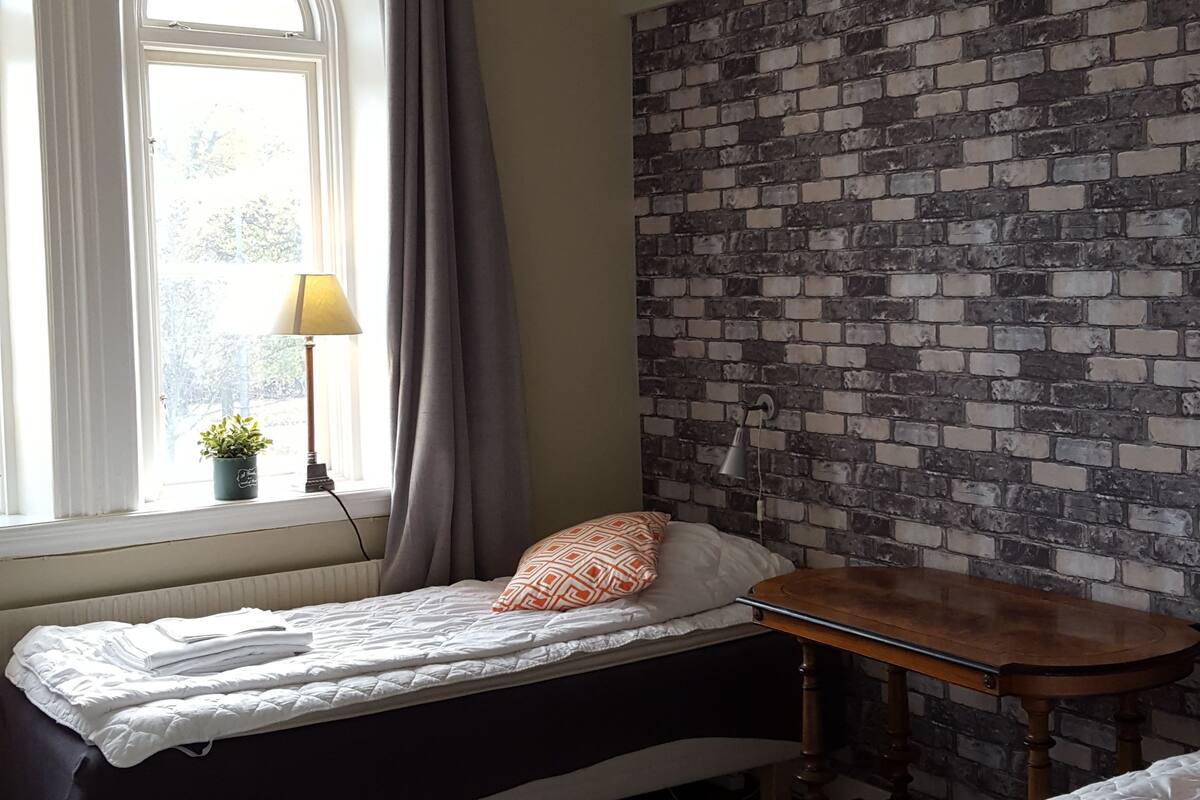 Ein Schlafzimmer mit zwei Betten, einer Wand mit Ziegeloptik, einer Chandelierleuchtre und einem fenster mit Vorhängen.