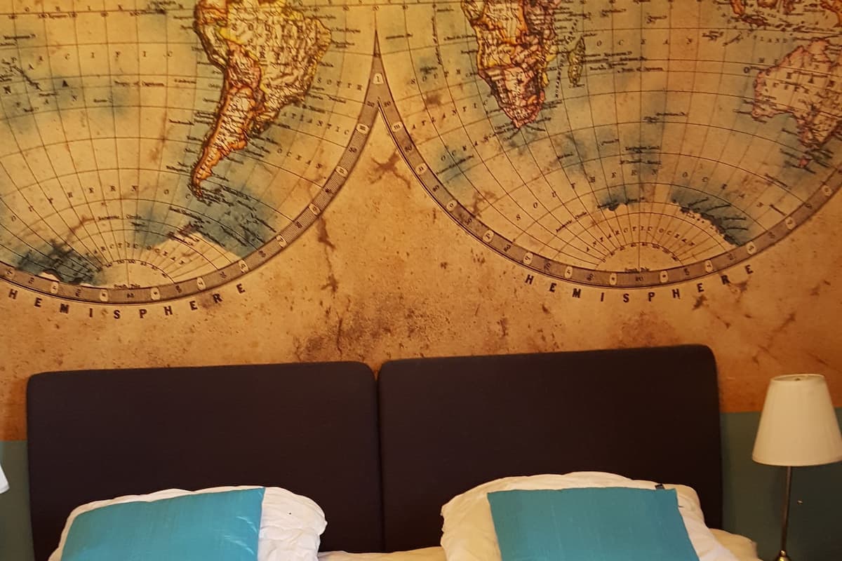 Ein Hotelzimmer mit einer großen Weltkarte an der Wand, einem Bett mit zwei Kissen und einer gesteppten Bettdecke.