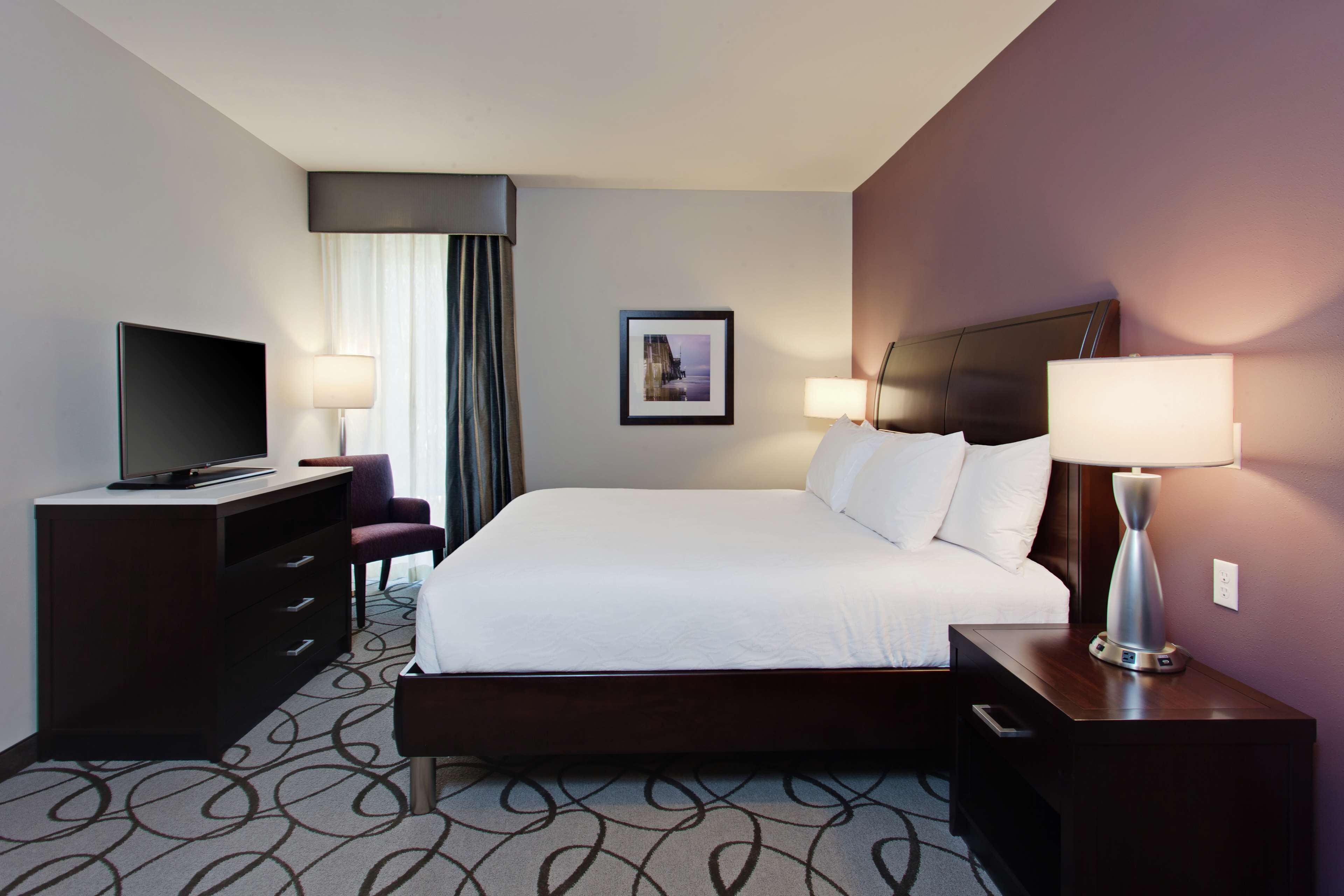 A hotel room with a bed, a TV, a desk, and a lamp.