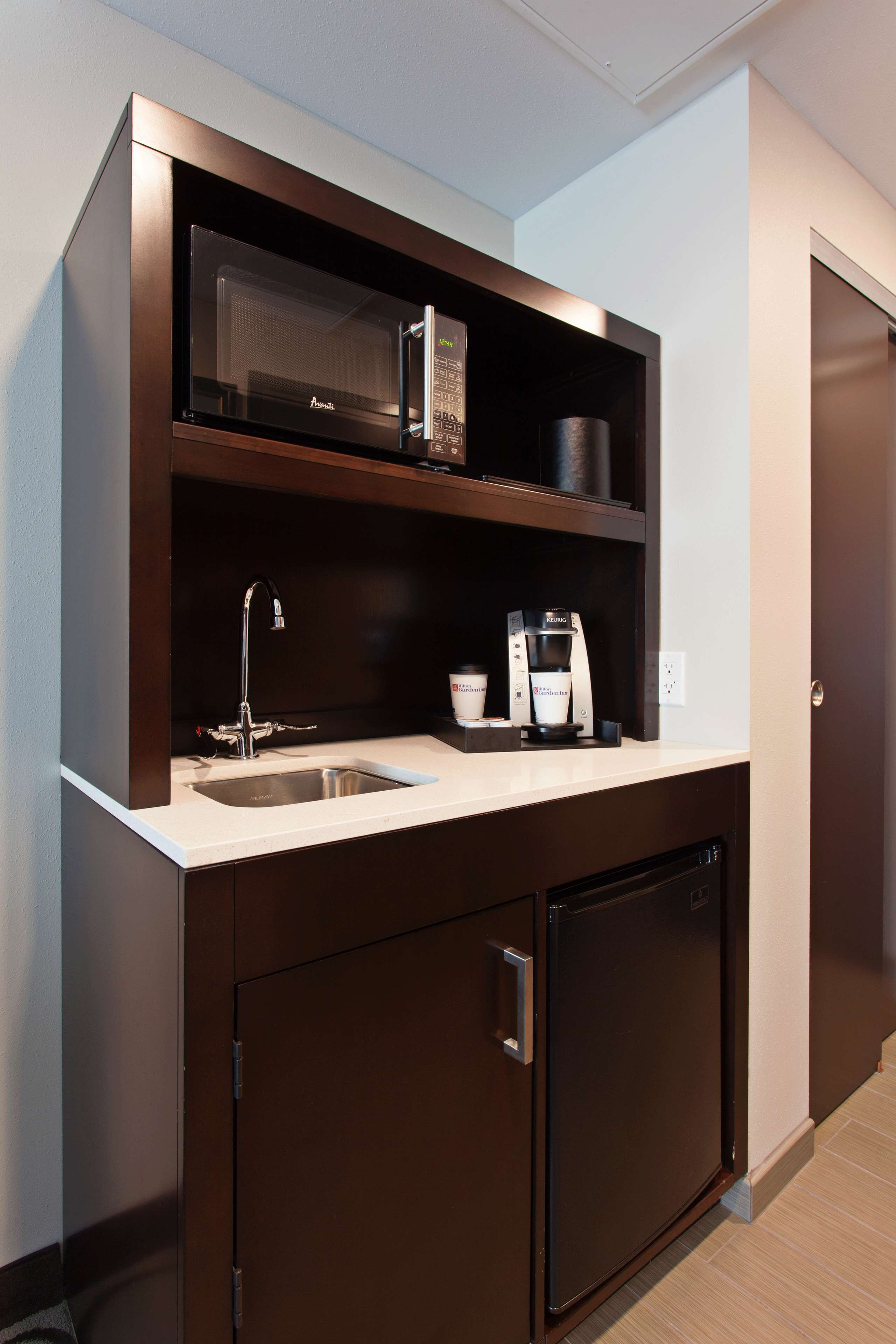 A compact kitchenette with a microwave, coffee maker, and sink.