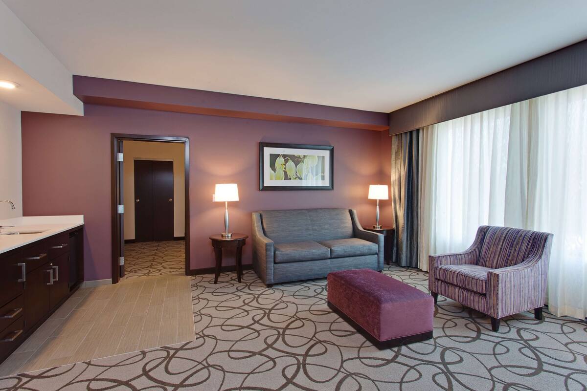 Ein Hotelzimmer mit Sofa, Ohrensessel, Hocker und einem Bild an der Wand.