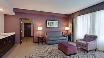 Una habitación de hotel con sofá, sillón, reposapiés y un cuadro en la pared.