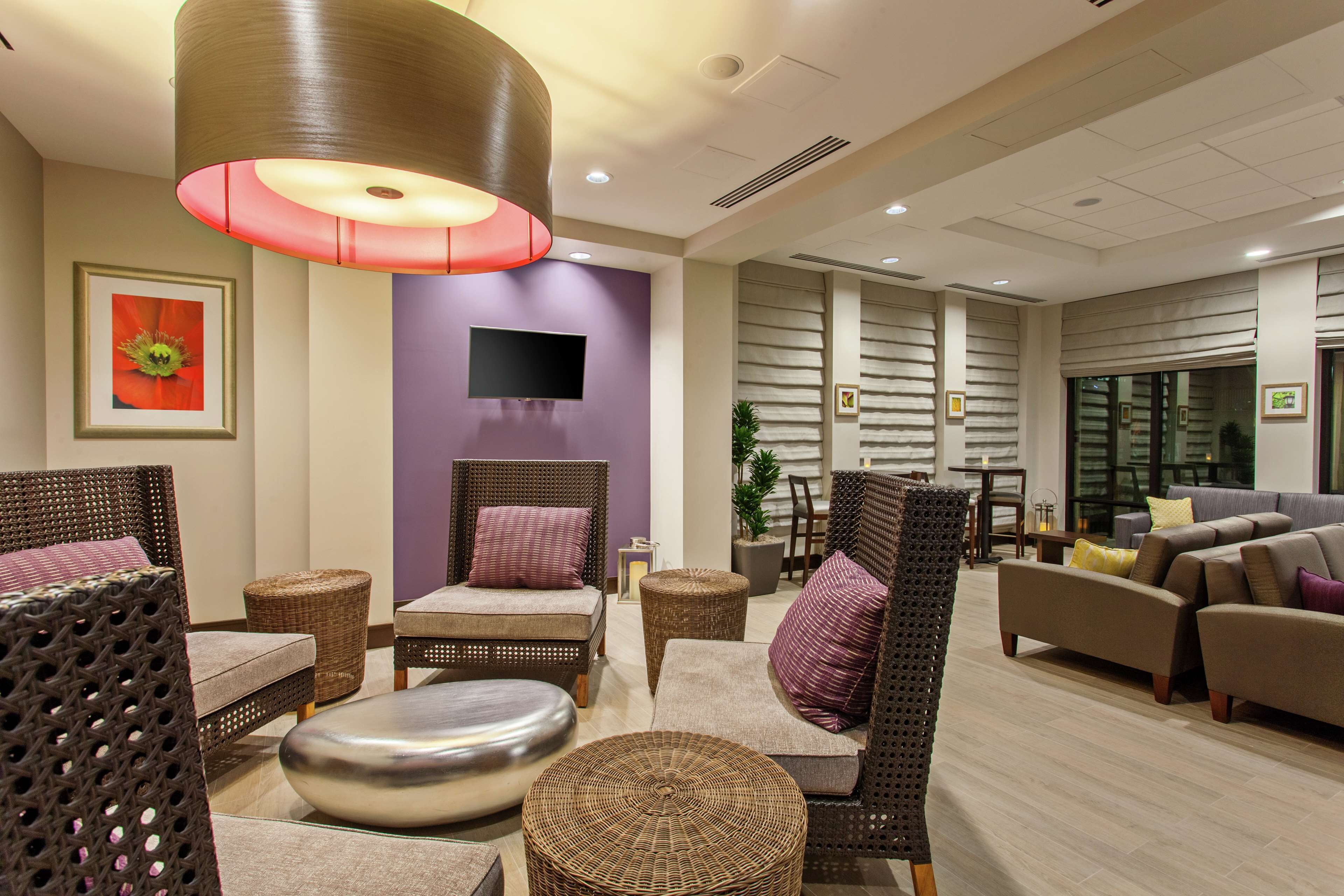 A modern hotel lobby with wicker furniture, a flat-screen TV, and a large red pendant light.