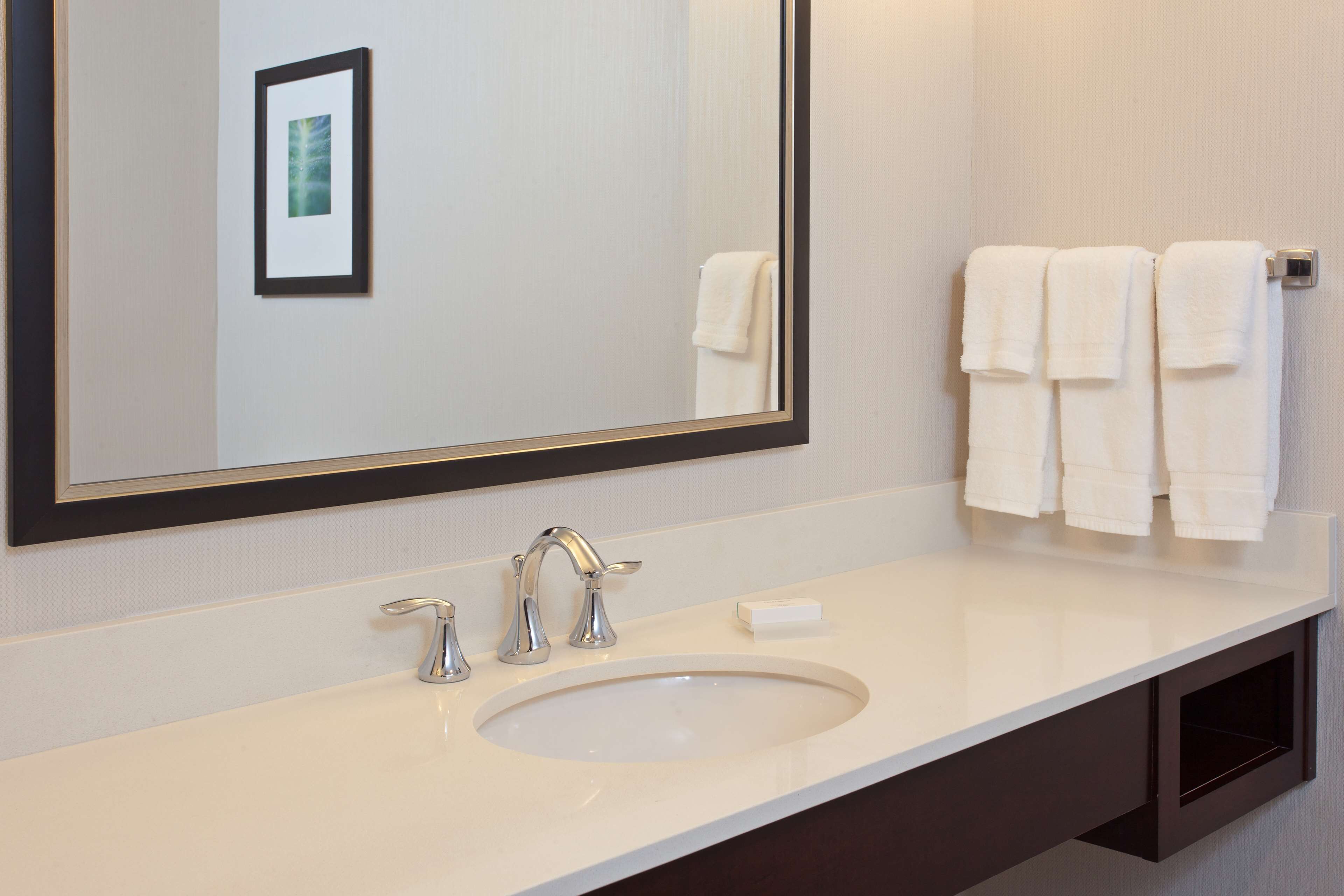 Une salle de bain avec un grand miroir, un lavabo, deux robinets et un porte-serviettes avec trois serviettes.