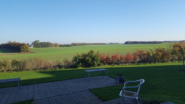 A patio area with a table and chairs, a grassy field, and a wind turbine in the distance.