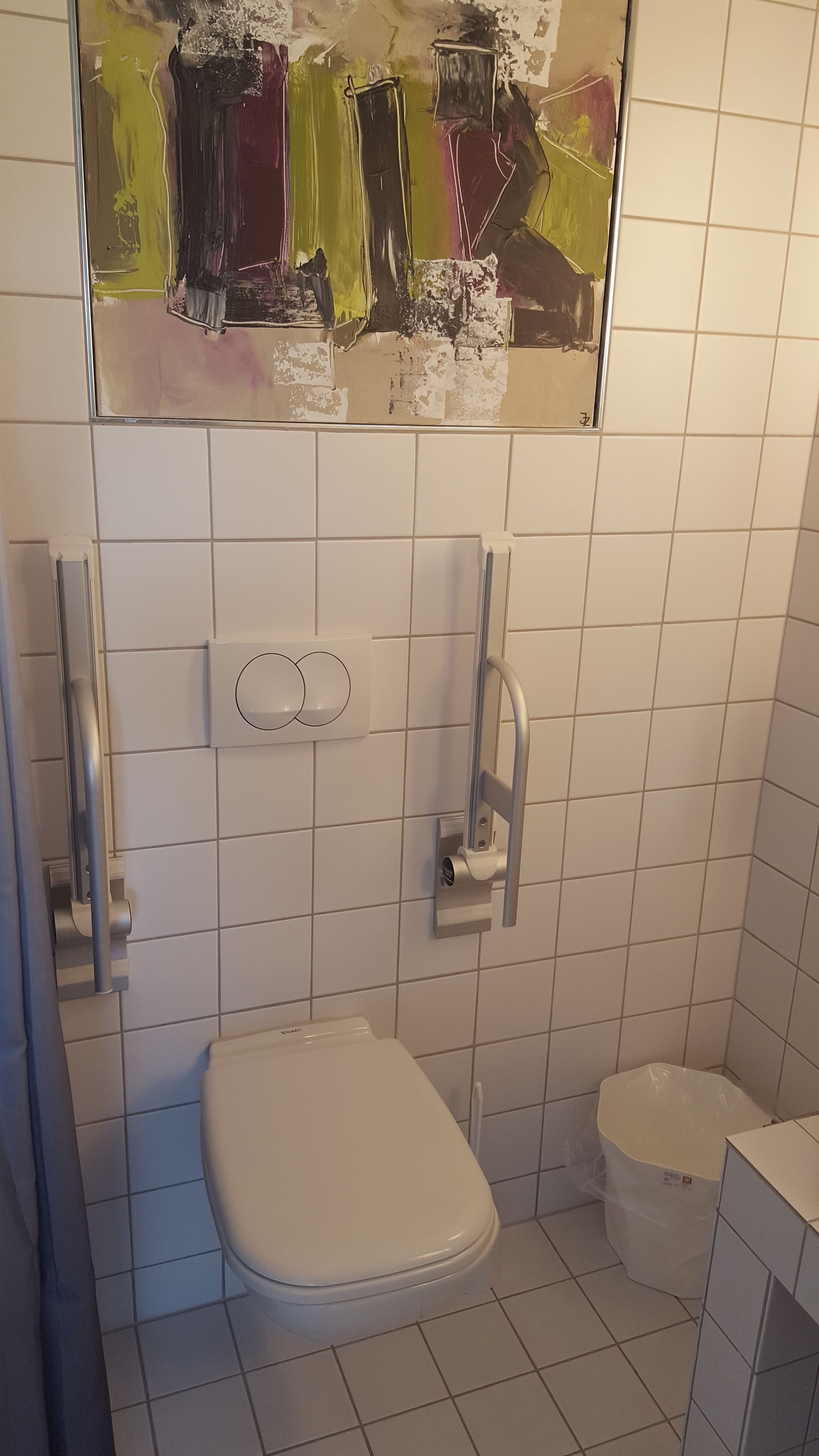 Un baño pequeño y funcional con inodoro, secamanos y cubo de basura.