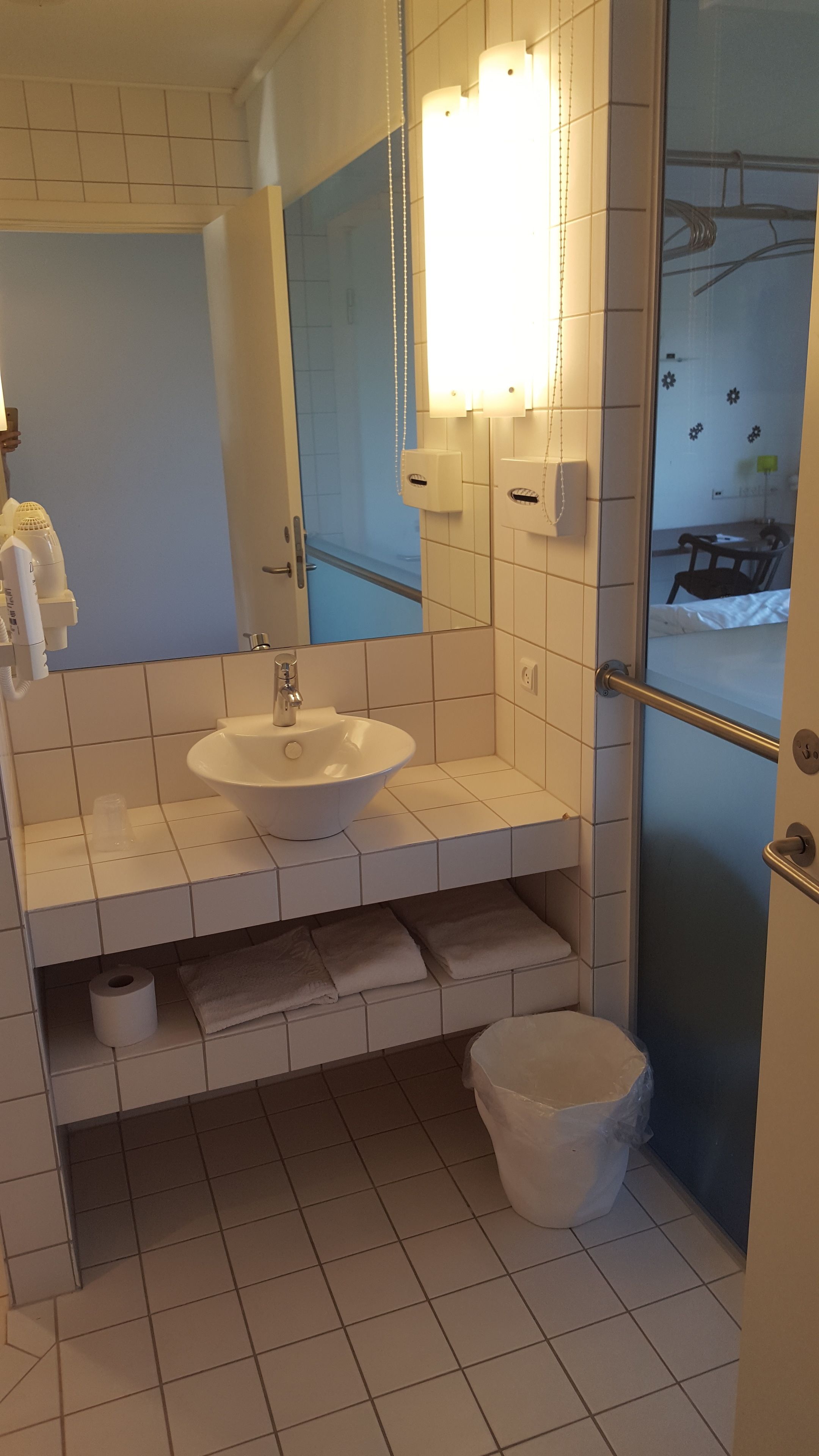 A bathroom with a white sink, mirror, and towel rack. There is a shower area with a glass door and a towel rack.