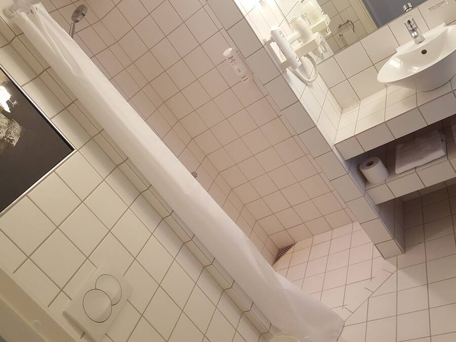 A bathroom with white tiles, a shower curtain, a sink, and a toilet.