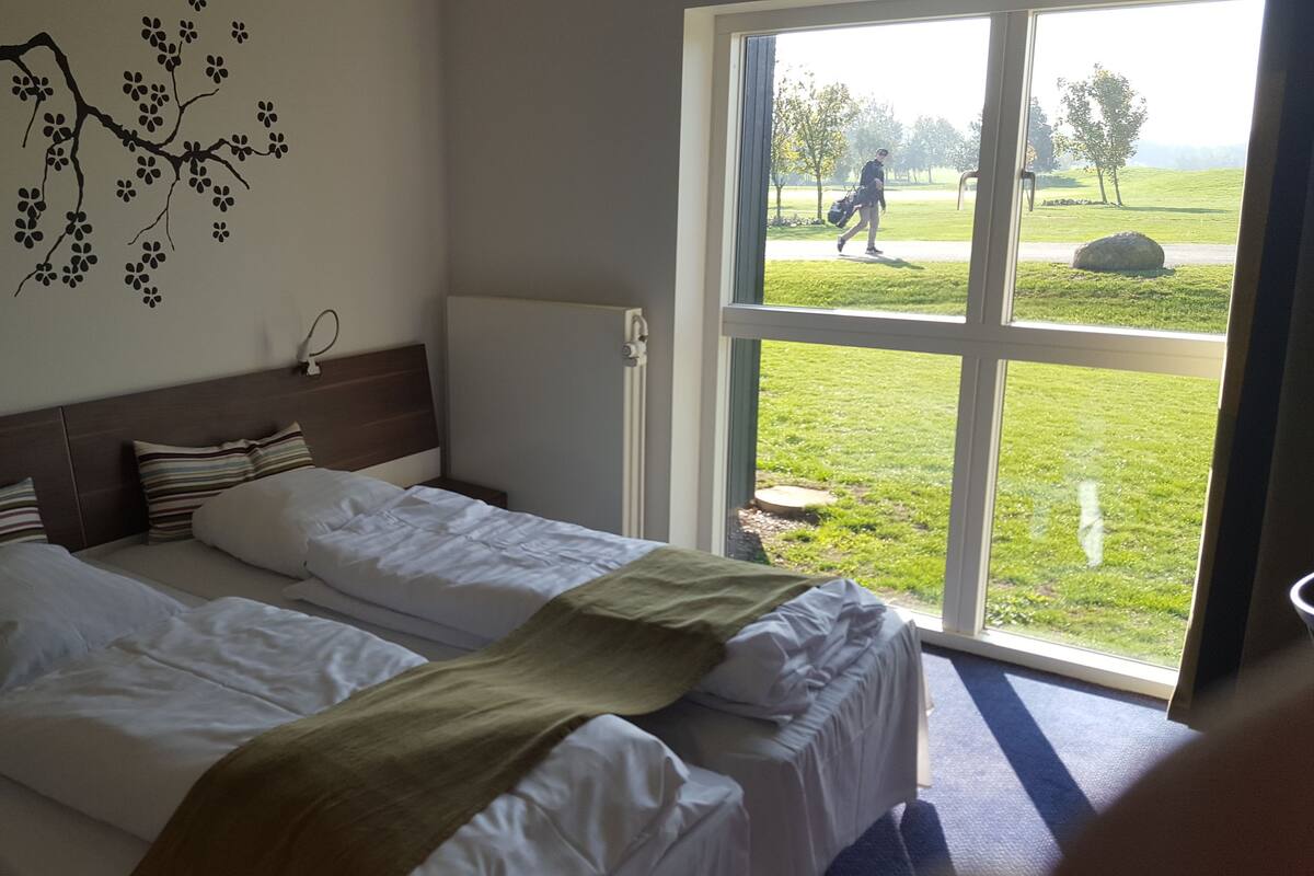 Une chambre d’hôtel avec deux lits, une vue sur l’extérieur grâce à une grande fenêtre et une décoration murale représentant une branche d’arbre.