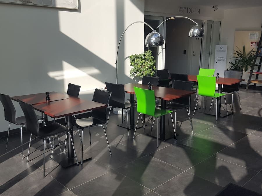 Ein Hotel-Empfangsbereich im modernen Design mit einer Rezeption, einem grünen Stuhl und einer Topfpflanze.