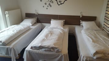 A hotel room with three single beds, each with white bedding and striped pillows.