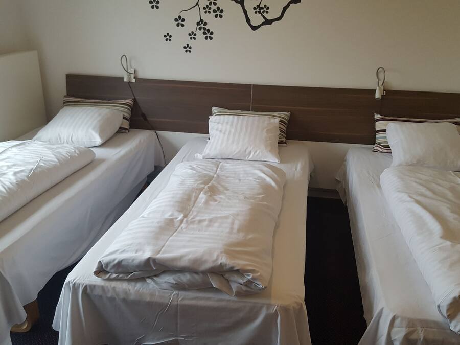 A hotel room with three single beds, each with white bedding and striped pillows.