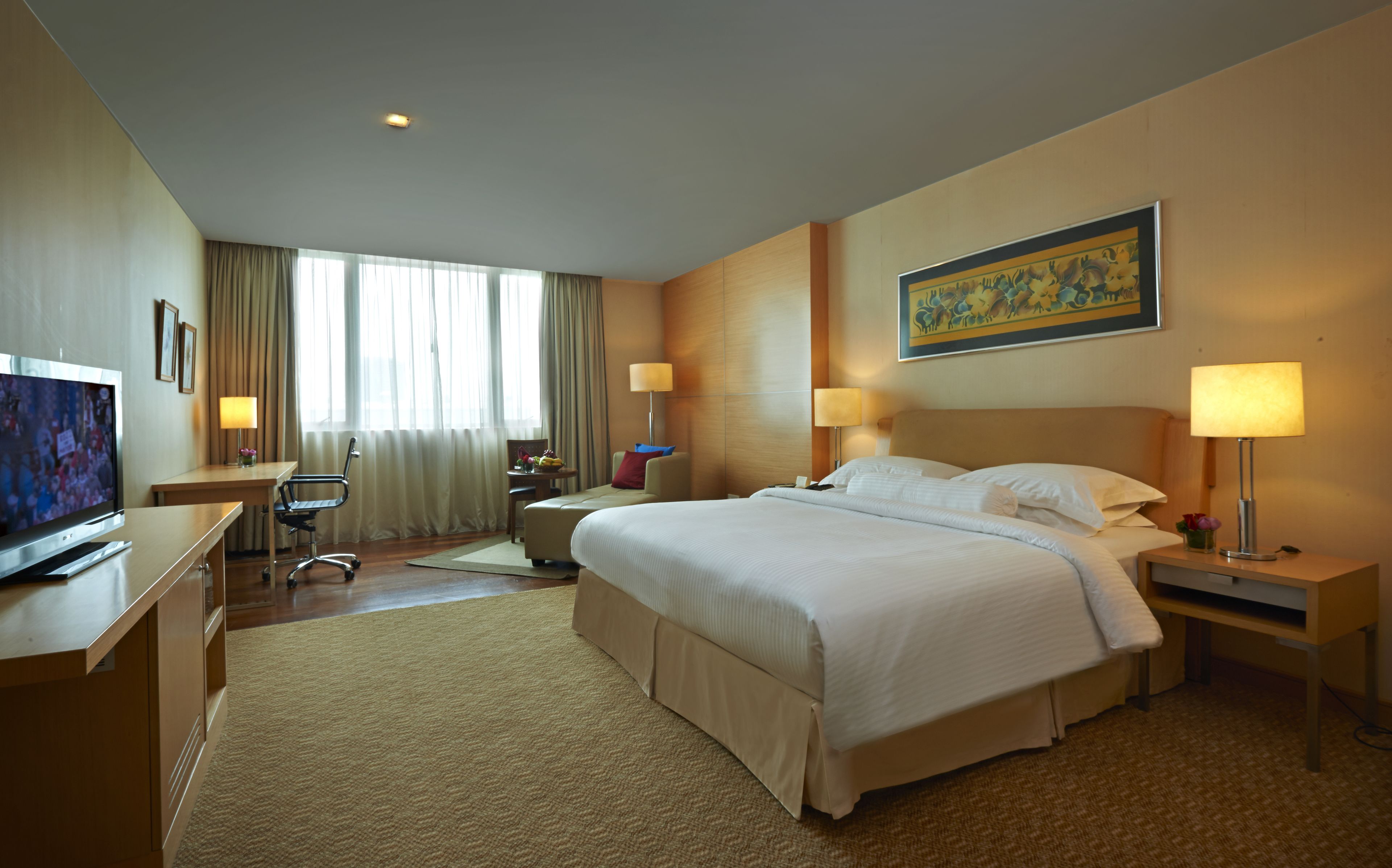 A hotel room with a bed, bedside lamps, a desk with a television, a chair, and a window with curtains.