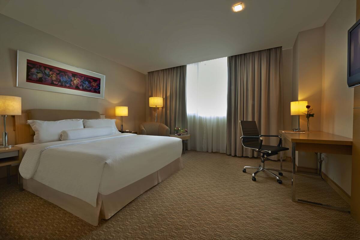 A hotel room with a large bed, a desk, two lamps, a chair, and a TV.