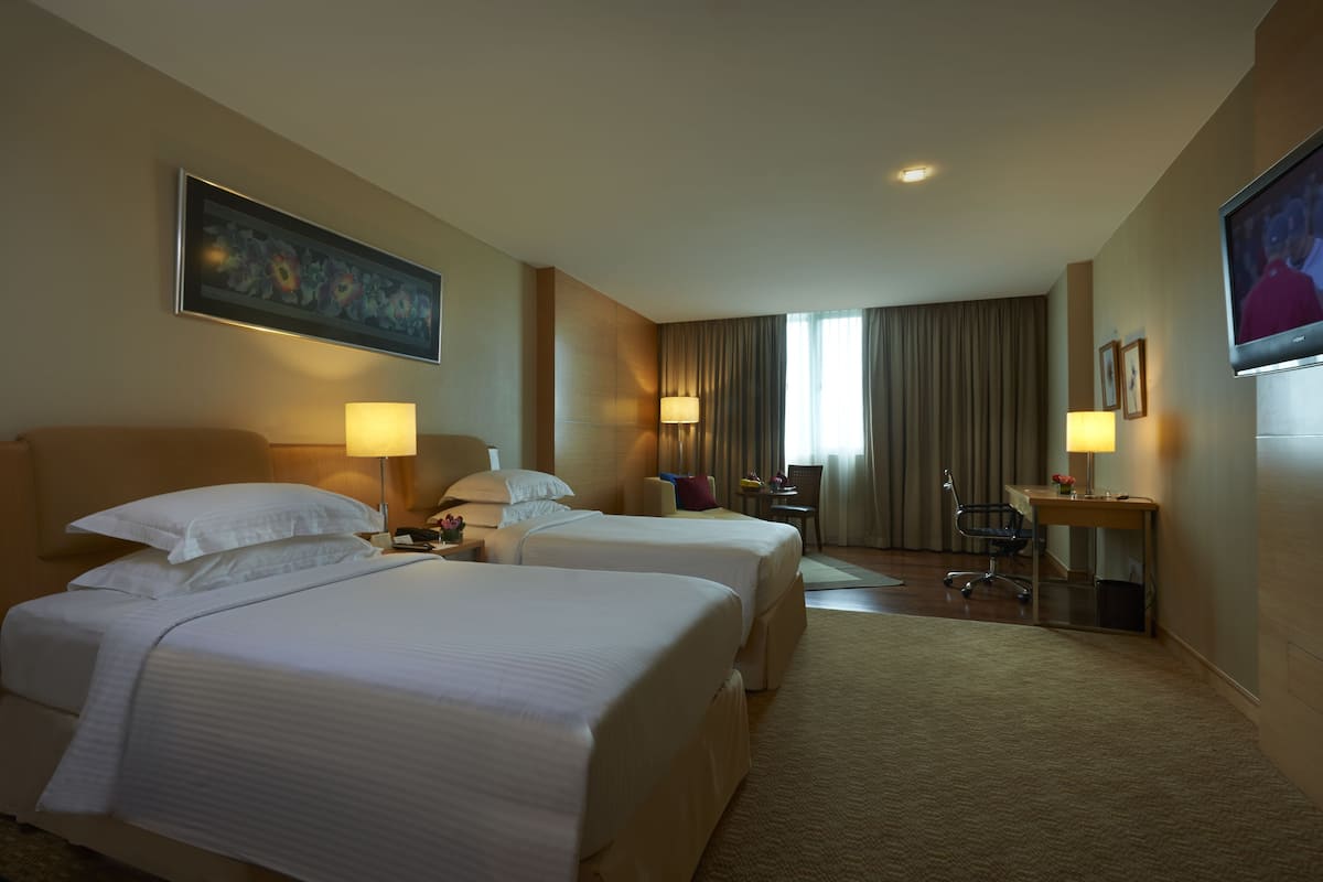 A hotel room with two beds, a desk, a chair, a TV, and a painting on the wall.