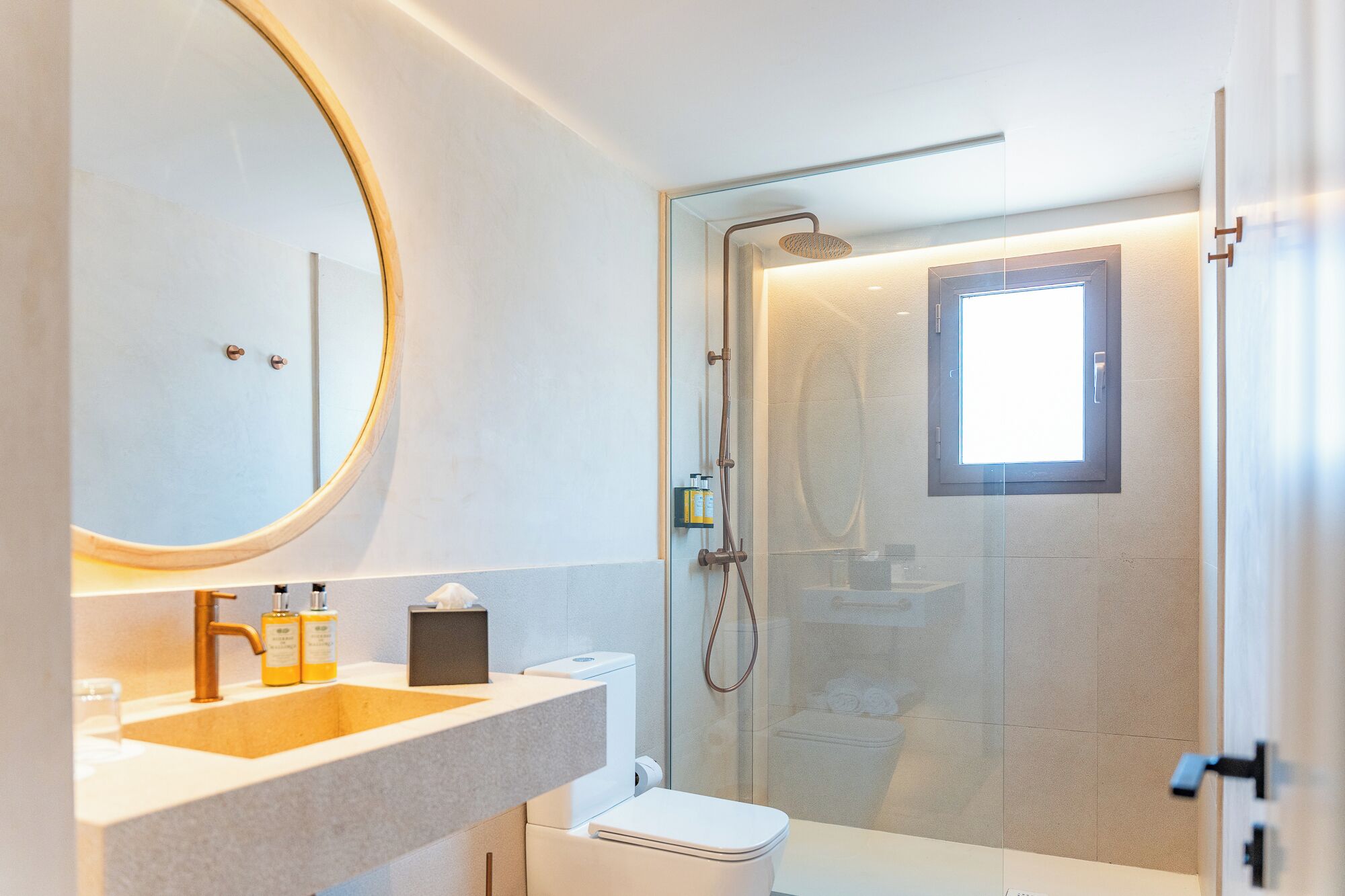 A modern bathroom with a round mirror, a sink, a toilet, and a shower enclosure.