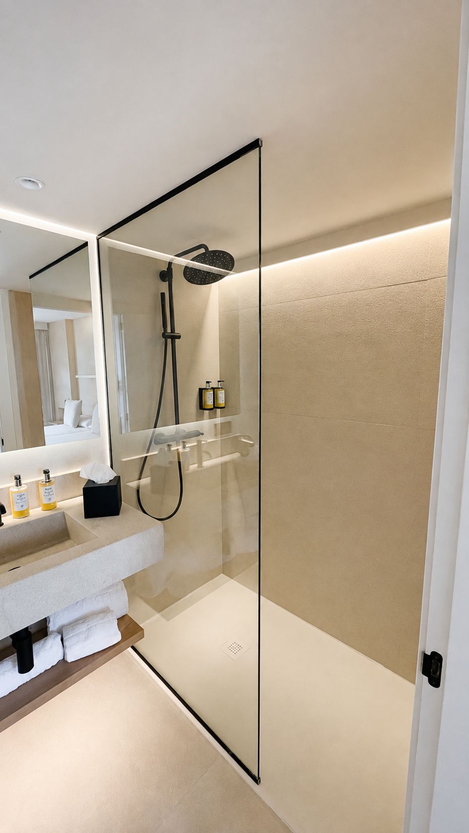 A modern bathroom with a glass-enclosed shower, a white sink with toiletries, and a large mirror.