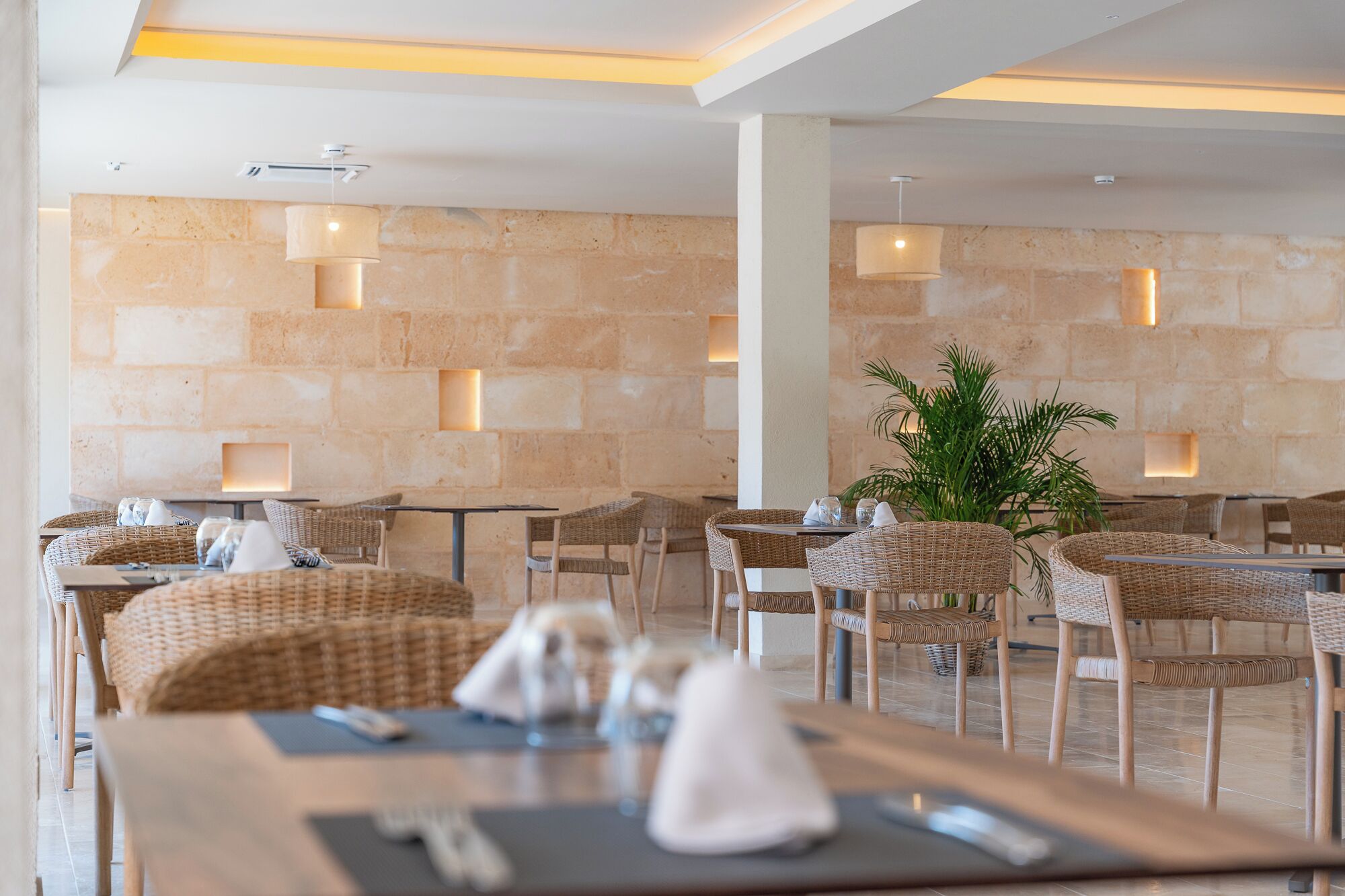 A restaurant with wicker furniture, stone walls, and recessed lighting.
