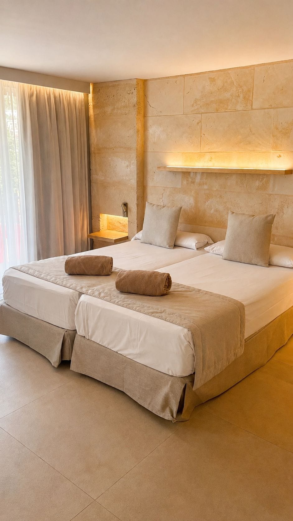 Una cama doble con cabecera, dos almohadas y una mesita de noche con lámpara.