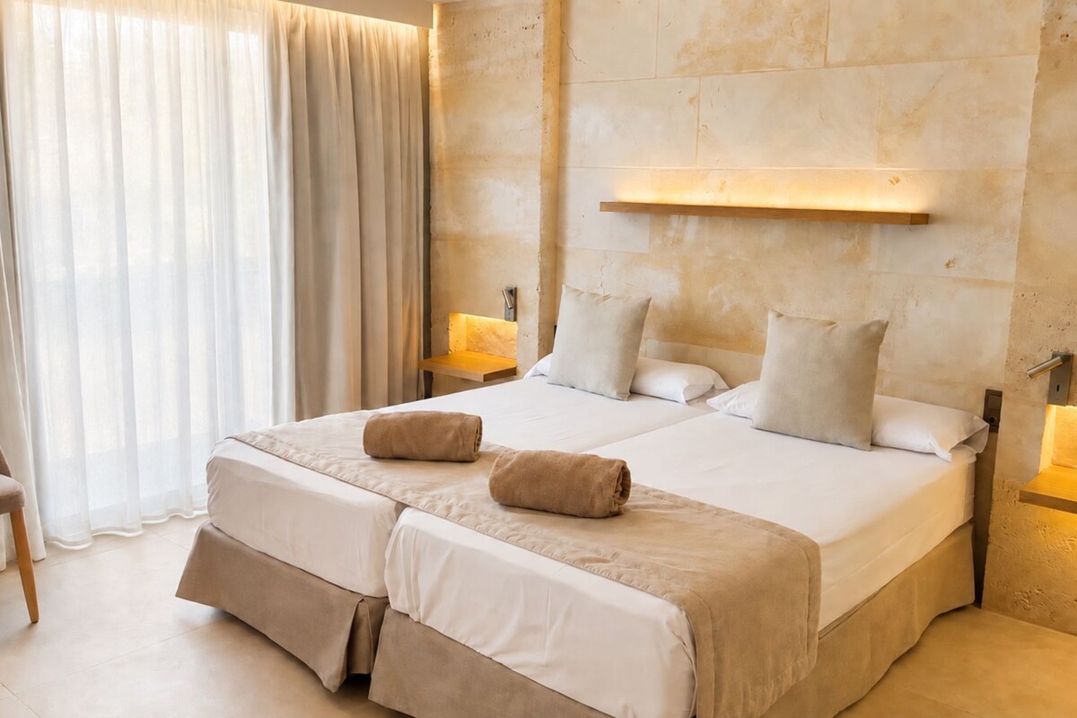 A hotel room with a large bed, two bedside tables, a chair, and a window with curtains.