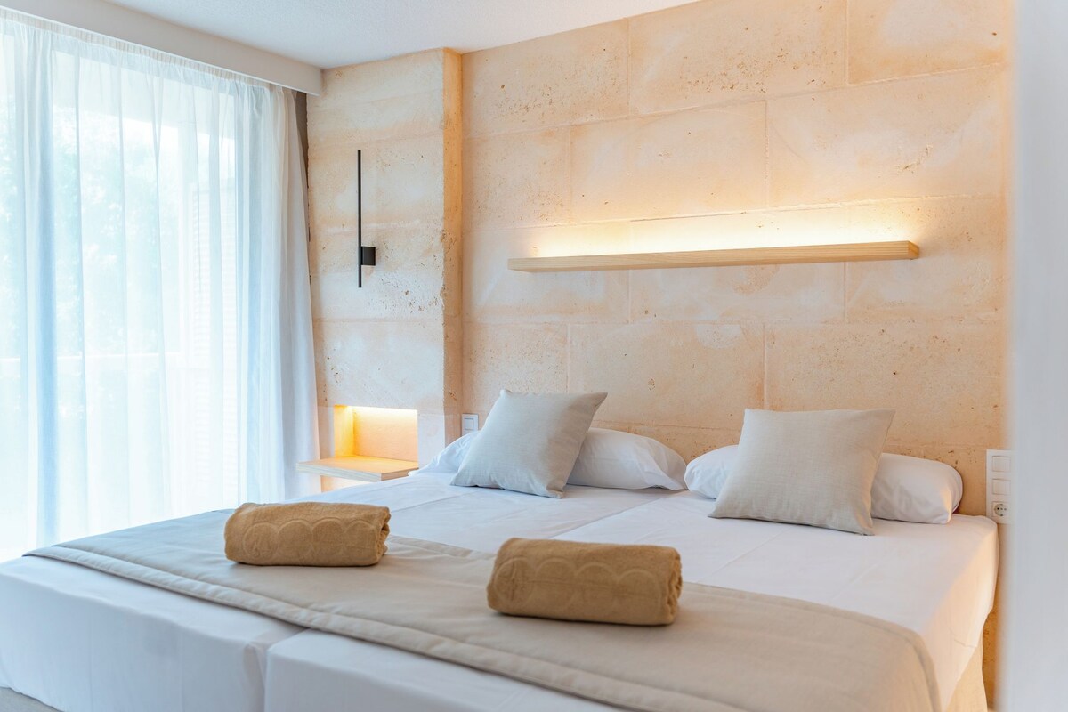 A hotel room with a large bed, two bedside lamps, and a window with sheer curtains.