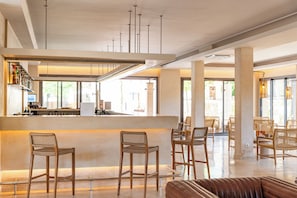 A modern bar area with high stools, a counter, and a view of the outdoor seating area. - Canyamel Sun Suites Hotel (Capdepera)