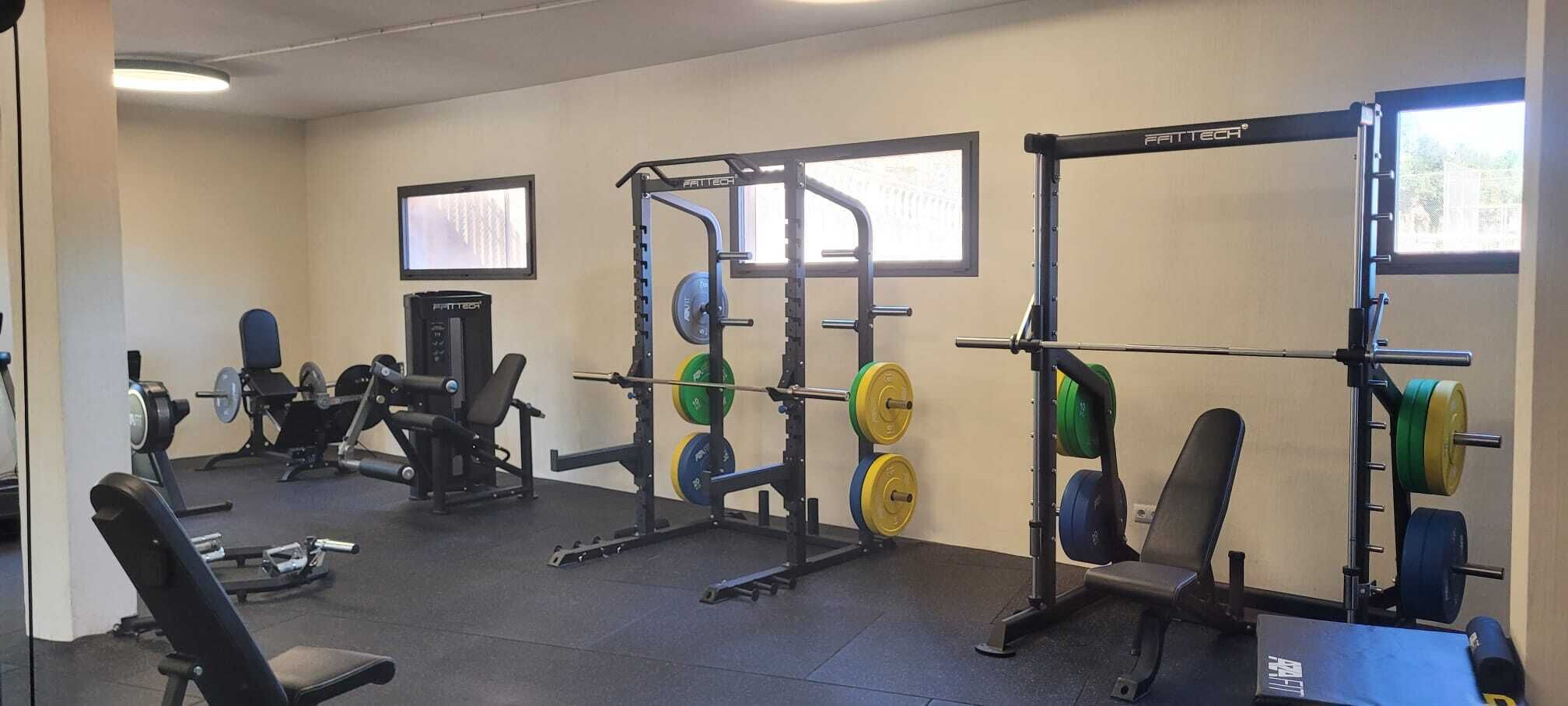 A gym with weightlifting equipment, benches, and a TV screen.