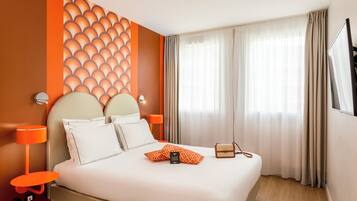 Une chambre d’hôtel avec un grand lit, deux tables de chevet, un téléviseur fixé au mur et une fenêtre avec des rideaux.