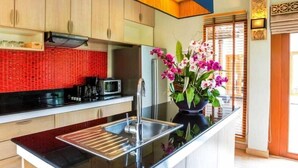 Une cuisine moderne avec des meubles en bois, un plan de travail noir, un évier en acier inoxydable et un pare-feu rouge.