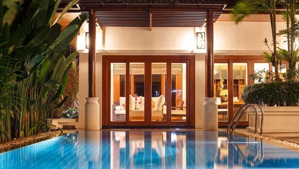 Une piscine dans laquelle se reflète un bâtiment, et une porte donnant sur une pièce.