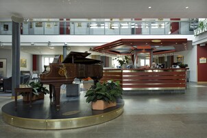 Um piano de cauda num hall de entrada com uma receção e uma escadaria.