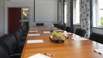 Ett konferensrum med ett långt bord i trä, svarta läderstolar, en projektorduk och en fruktskål på bordet.