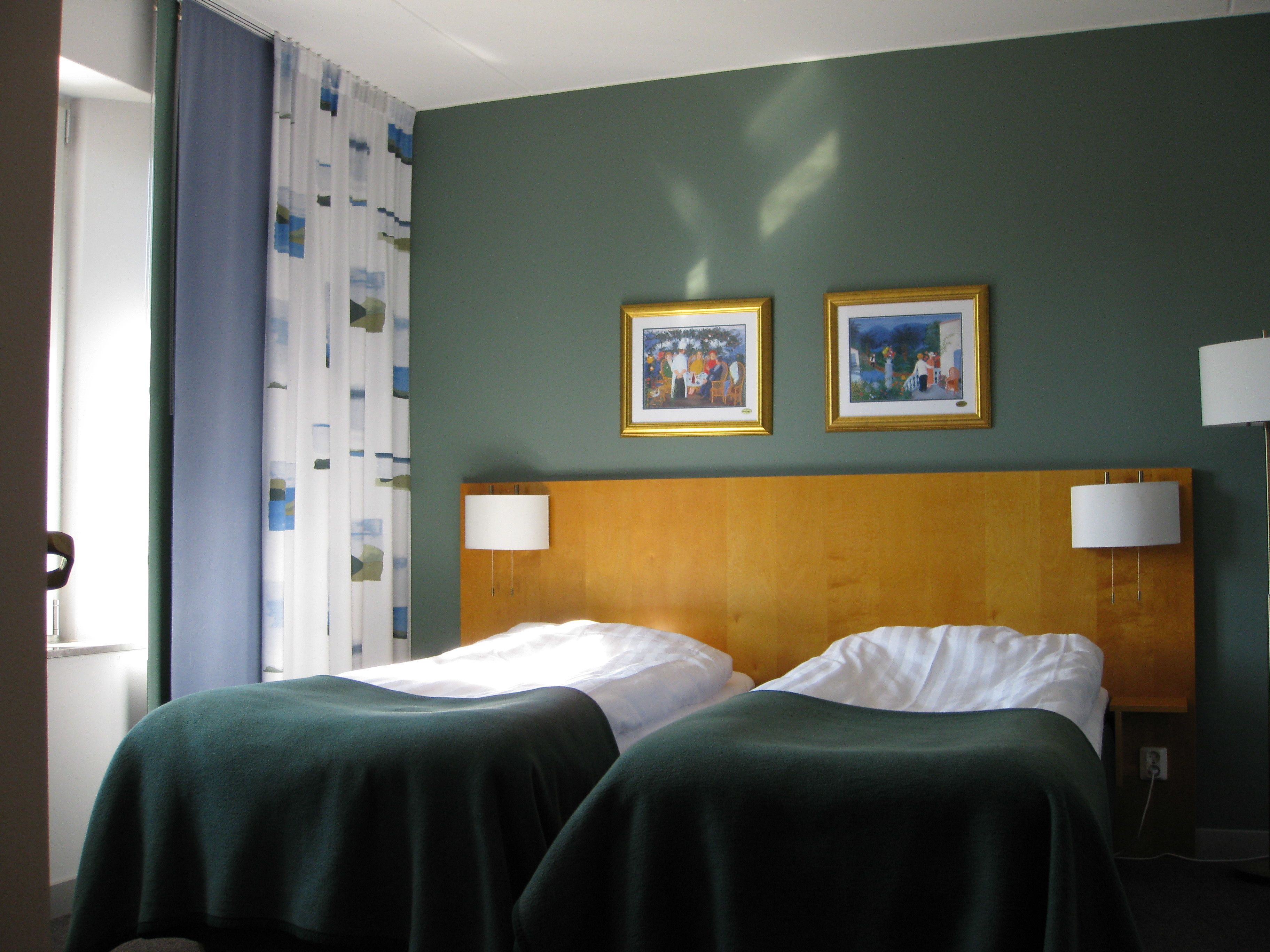 A hotel room with two beds, a wooden headboard, and two framed pictures on the wall.