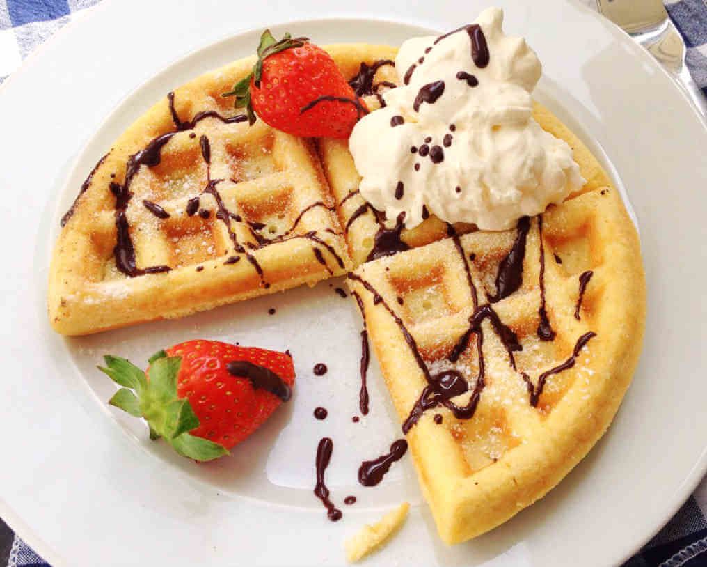 Um prato com waffles, chantilly, calda de chocolate e morango.