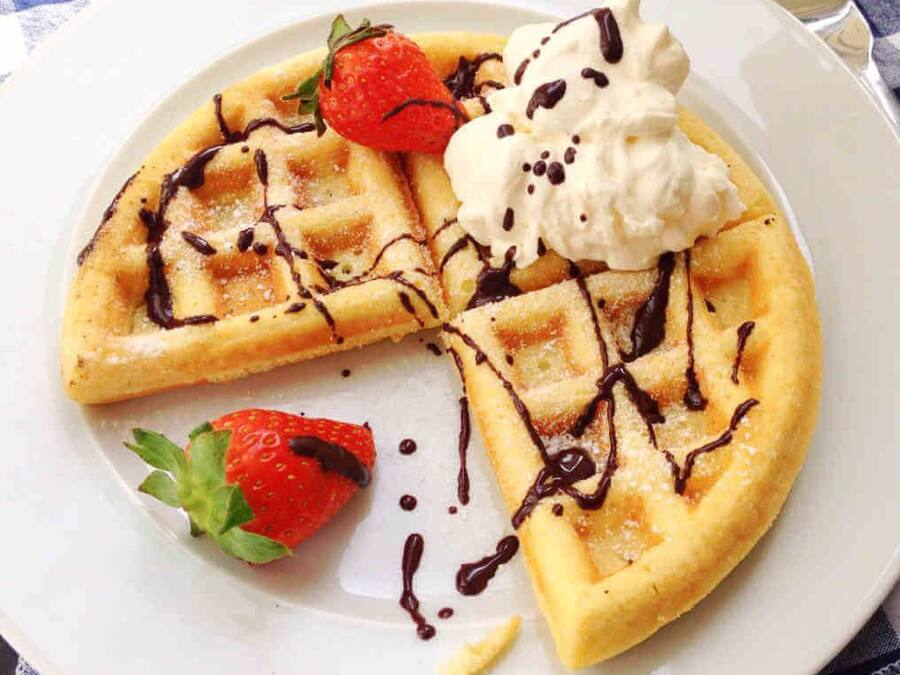 A plate with waffles, whipped cream, chocolate syrup, and a strawberry.